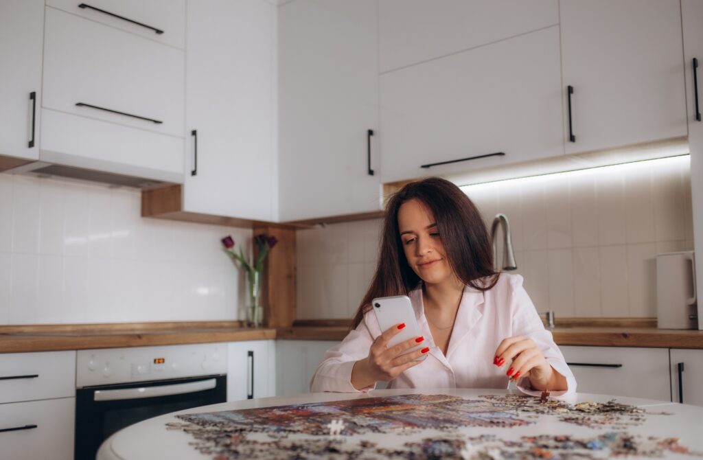 a woman in the kitchen is doing puzzles while holding the phone in her hand